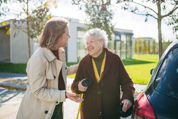 Granddaughter teaching senior woman how to charge new electric car. Progressive grandmother...