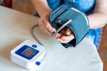 Senior woman finish to check blood pressure level at home, older female suffering from high blood...