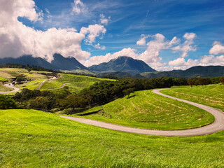 the nature mountain ridge landscape view is a green grass meadow field and highland hill mountain countryside road with white cloud cloudscape on a blue beautiful bright sunlight sunny sky background