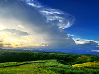 the nature mountain ridge landscape sunrise or sunset view is a green grass meadow and highland hill glen mountain with white cloud cloudy cloudscape on a blue beautiful bright sunlight sky background