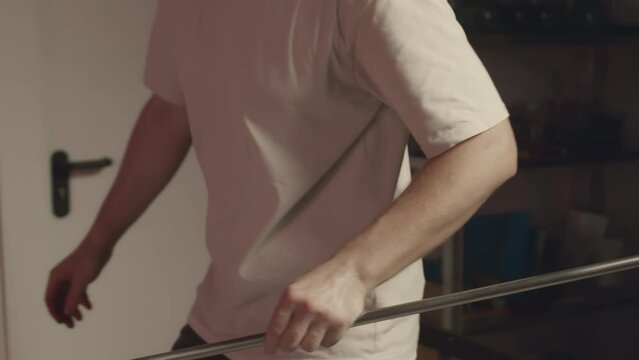 Following medium shot of young Caucasian male gaffer heating glass piece on pipe in furnace then molding its shape with tweezers while working at glass making factory