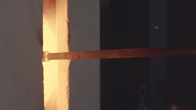 Closeup shot of unrecognizable glassblowing master melting glass bubble on pipe in heated furnace at glass making workshop