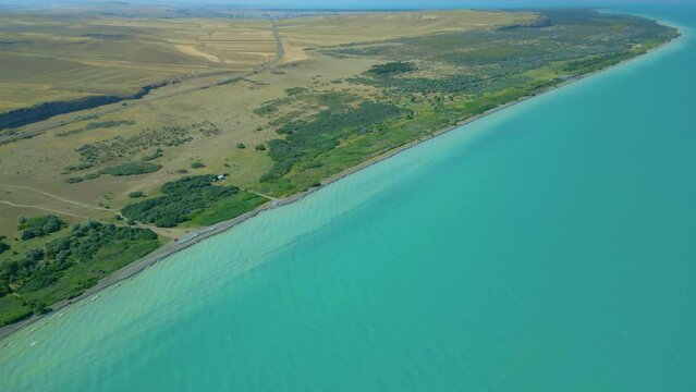 An aerial view of a large blue azure sea lake in clear sunny weather. Shoreline with beaches, overgrown with trees. Drone video, flying in an arc. Lake Sevan, Armenia.