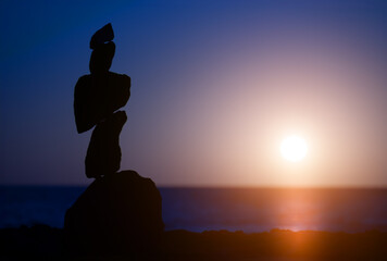 balancing stacked stones against the backdrop of the setting sun on the seashore