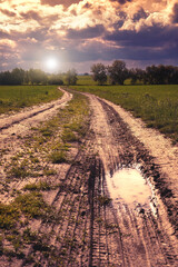 Wheel off-road track in a countryside landscape with a muddy road. Extreme path rural dirt. Beautiful sunset.
