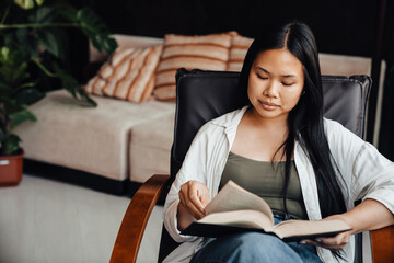 Beautiful woman reading book while sitting on chair at home