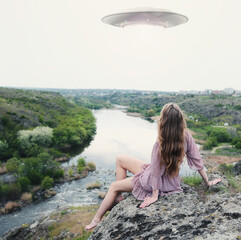 A girl sitting on a rock above the river watching a flying UFO. 