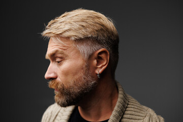 Profile of blonde and bearded man in knitted cardigan standing isolated on grey  - obrazy, fototapety, plakaty