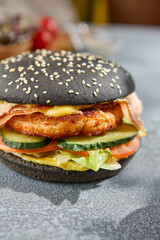 Macro vertical image capturing intricate details of a chicken and bacon burger on a black bun. The gray concrete background features harsh, aesthetic shadows