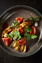 Close-up top view in a vertical format, magnifying the details of roasted eggplant served with tomatoes, cilantro, and cheese on an elegant stone plate