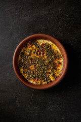 Vertical top perspective of crème brûlée with pistachio, served in a clay bowl, showcasing gourmet aesthetics on a dramatic black canvas