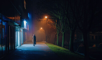 A lone walker on illuminated city streets at midnight. - 677520346