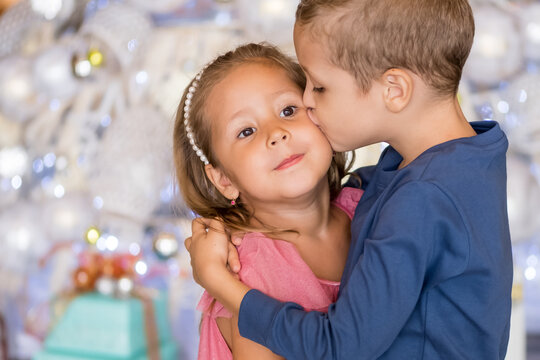 Cute boy standing by Christmas tree, hugging and kissing little sister. Merry Christmas and happy holidays