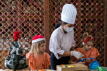 Children decorating Christmas biscuits and gingerbread cookies in kitchen together with chef. Kids cooking class. Merry Christmas and happy holidays