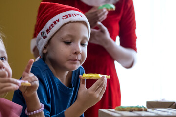 Children decorating Christmas biscuits and eating gingerbread cookies in kitchen together with Mrs. Claus. Kids cooking class. Merry Christmas and happy holidays