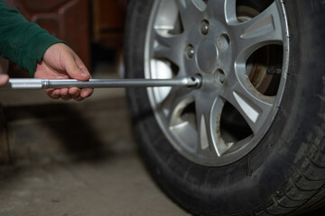 A man in a garage unscrews a car wheel with a key. The car stands on a jack while a man repairs a...