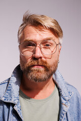 Obraz premium Portrait of blonde and bearded man in eyeglasses and denim jacket looking at camera isolated on grey 