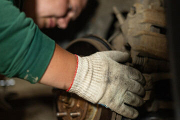 A man in work gloves repairs a wheel on a car in a garage. A man replaces a broken part on his car...