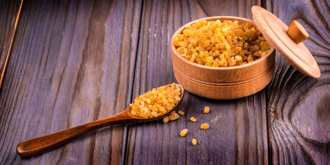 The Wooden scoop spoon and bowl full of brown cane sugar with pinch of sugar spilled around on wooden table, top view