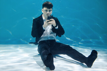 Artistic business concept. Man sitting with phone underwater on blue background