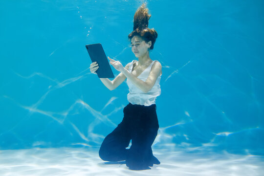 A woman uses a tablet while she is at the bottom underwater. Creative concept