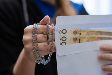 Modląca się kobieta trzyma w dłoni kopertę z pieniędzmi w dużych nominałach 