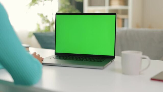 Close-up image shows woman using laptop, with hands on keyboard while gazes at computer screen, chroma key green screen