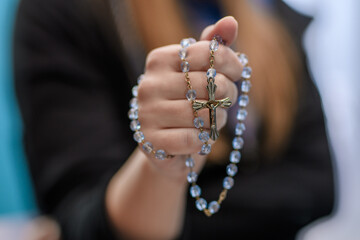 Dziewczyna katoliczka trzyma w dłoni różaniec z krzyżem  - obrazy, fototapety, plakaty