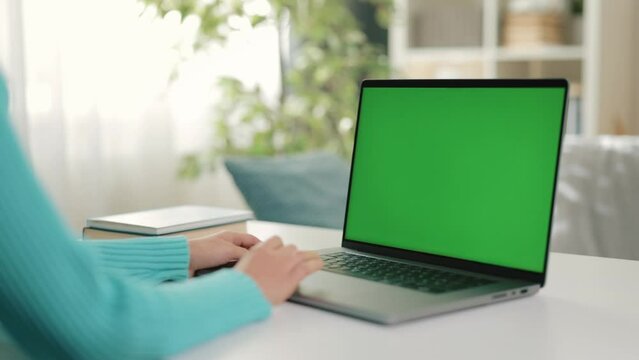 Close-up woman using laptop, with hands actively typing on keyboard while sending messages, backdrop features green screen with chroma key