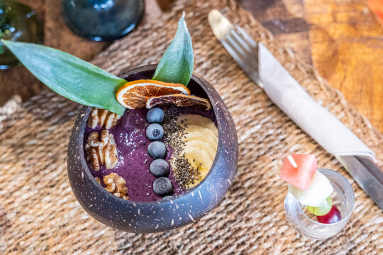 A wholesome breakfast with this stunning image featuring a delicious Açaí bowl adorned with luscious blueberries and crunchy nuts, presented within a unique coconut shell cup
