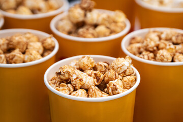 delicious sweet caramel brown popcorn. in a yellow orange glass close-up. boxes of popcorn on sale on the counter in the store. Paper bucket with popcorn, concept of watching TV or cinema.
