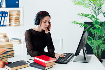 business woman office worker in headphones in the office at a desk with books in the office with a laptop