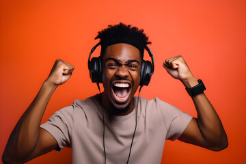 studio portrait of happy gamer black man wearing headphones celebrating on orange background
