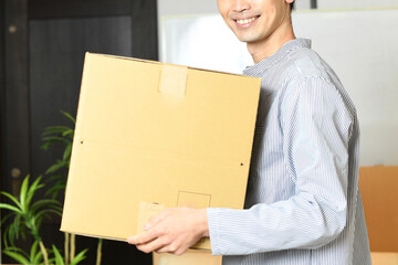 段ボール箱を運ぶ私服姿の若いアジア人男性