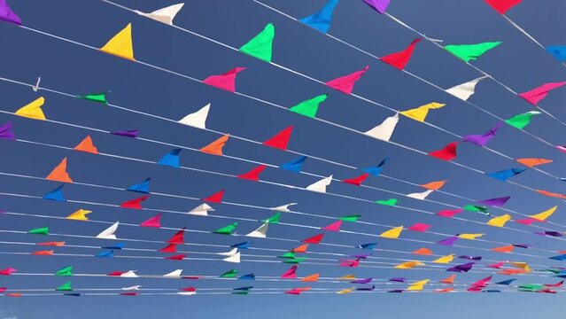 Multicolored triangular small flags to celebration party waving on the wind against blue sky.Street holiday concept for design.