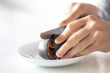 A woman cuts a passion fruit into two halves.