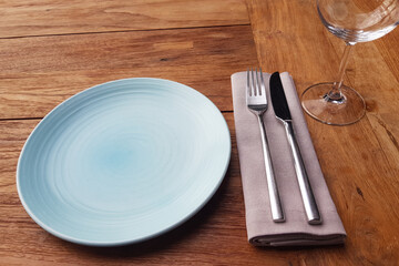 Set of blue empty plate, napkin, fork and knife on brown wooden table in restaurant