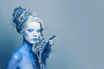 Beautiful cool cold woman with blue and white body art, carnival makeup and hairstyle on light blue...