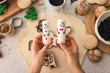 A snowman made of marshmallows in female hands in the kitchen, top view.