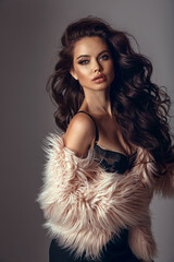 Beautiful woman portrait with long wavy hair and vogue style makeup in pink fur coat isolated on studio grey backround. Gorgeous chic girl model in sexy outfit. - 677550365