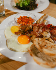Full English breakfast on a plate with fried eggs, sausages, bacon, beans, toasts. Top view. Breakfast in restaurant