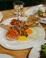 Full English breakfast on a plate with fried eggs, sausages, bacon, beans, toasts. Top view. Breakfast in restaurant