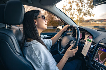 Naklejka premium An attractive young woman driving a car uses a navigator.