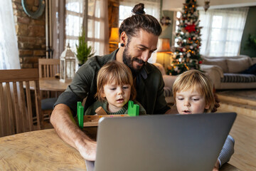 Fatherhood and remote business. Happy young single dad working at home while kids play next to him