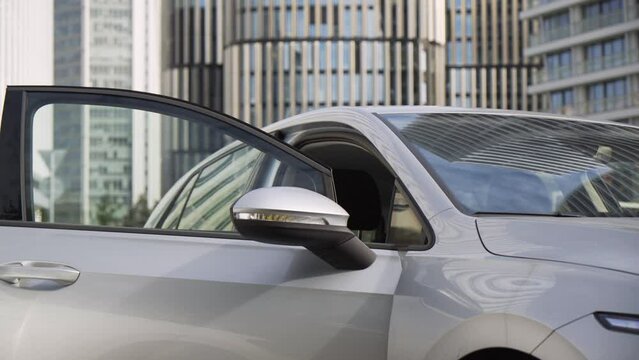A young beautiful Caucasian businesswoman gets out of a car - office buildings in the background
