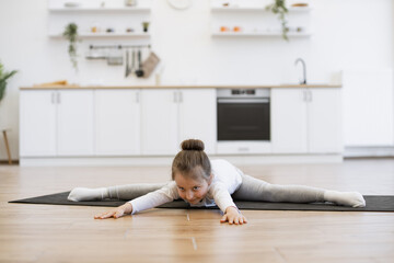 Caucasian preschool girl 5 years old in sports wear is engaged in gymnastics at home in the kitchen...