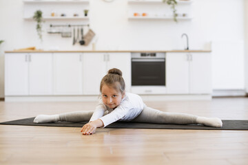 Caucasian preschool girl 5 years old in sports wear is engaged in gymnastics at home in the kitchen...