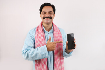 Portrait of Indian farmer man in rural India concept. Funky expressions white background. Cheerful farmer showing, pointing at mobile phone screen using advance wireless technology.