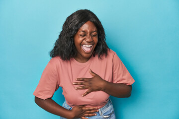 Young african american curvy woman laughs happily and has fun keeping hands on stomach.