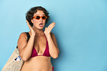 Young woman in bikini with beach bag surprised and shocked.